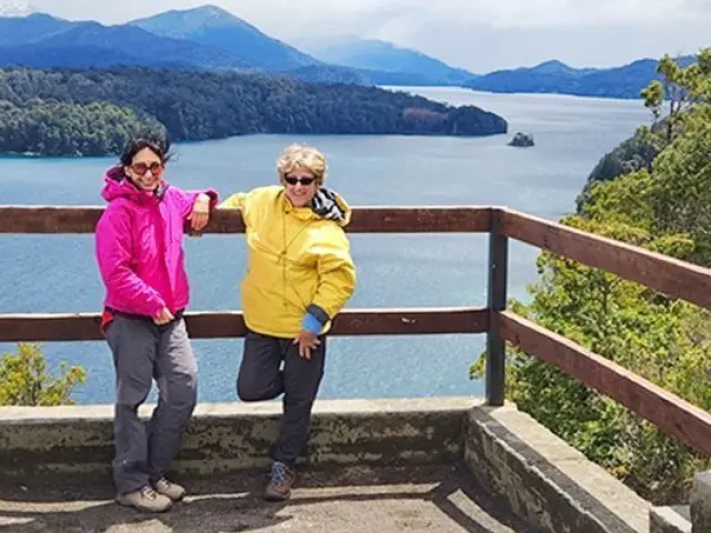Two guests at a lookout above a lake and forested mountains.